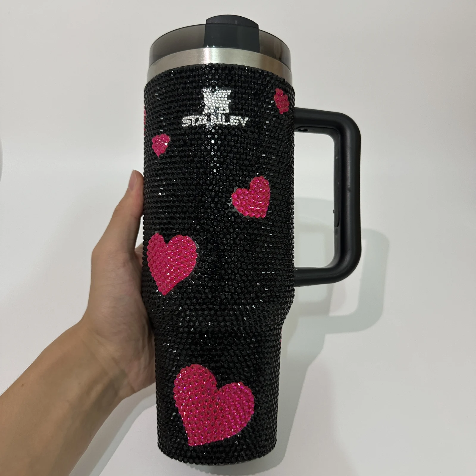 Handheld view of the black rhinestone tumbler with pink heart decoration